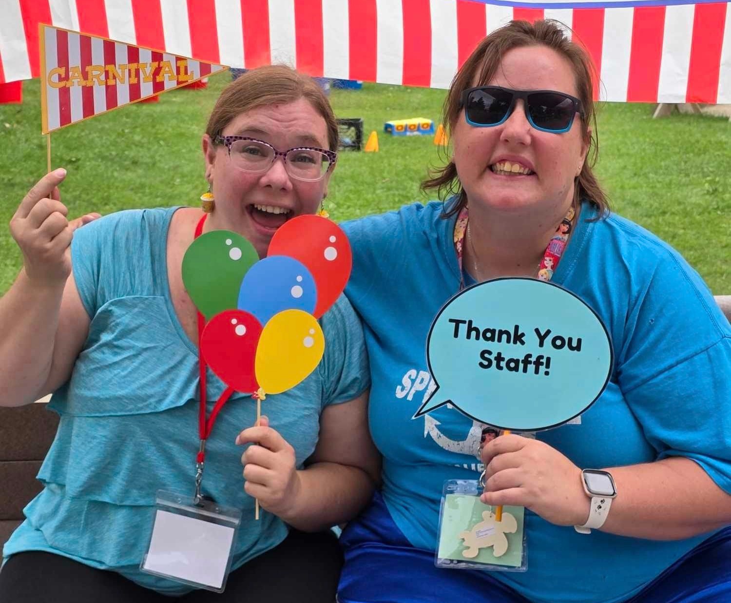 Two women smiling one with a sign that says thank you staff
