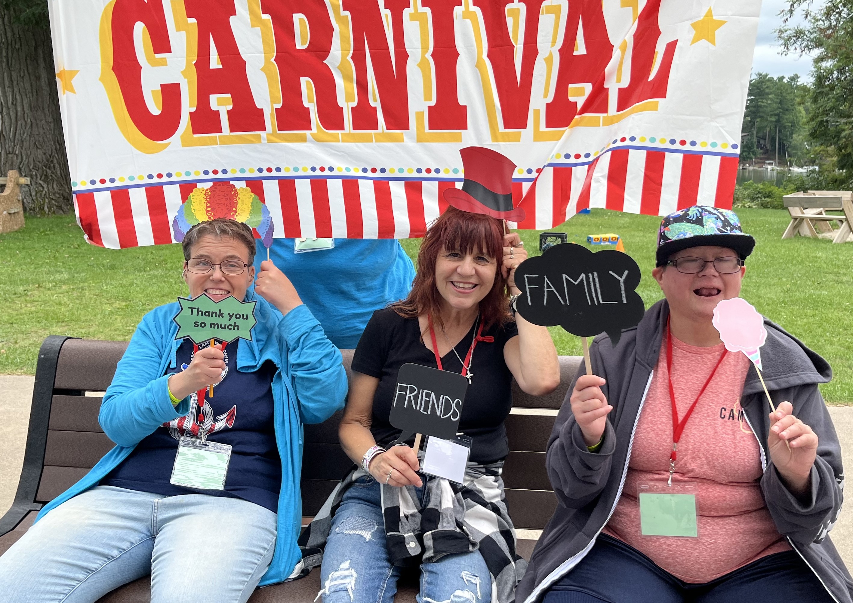 A photo of three woman in a carnival photo booth area with fun signs reading family friends thank you so much