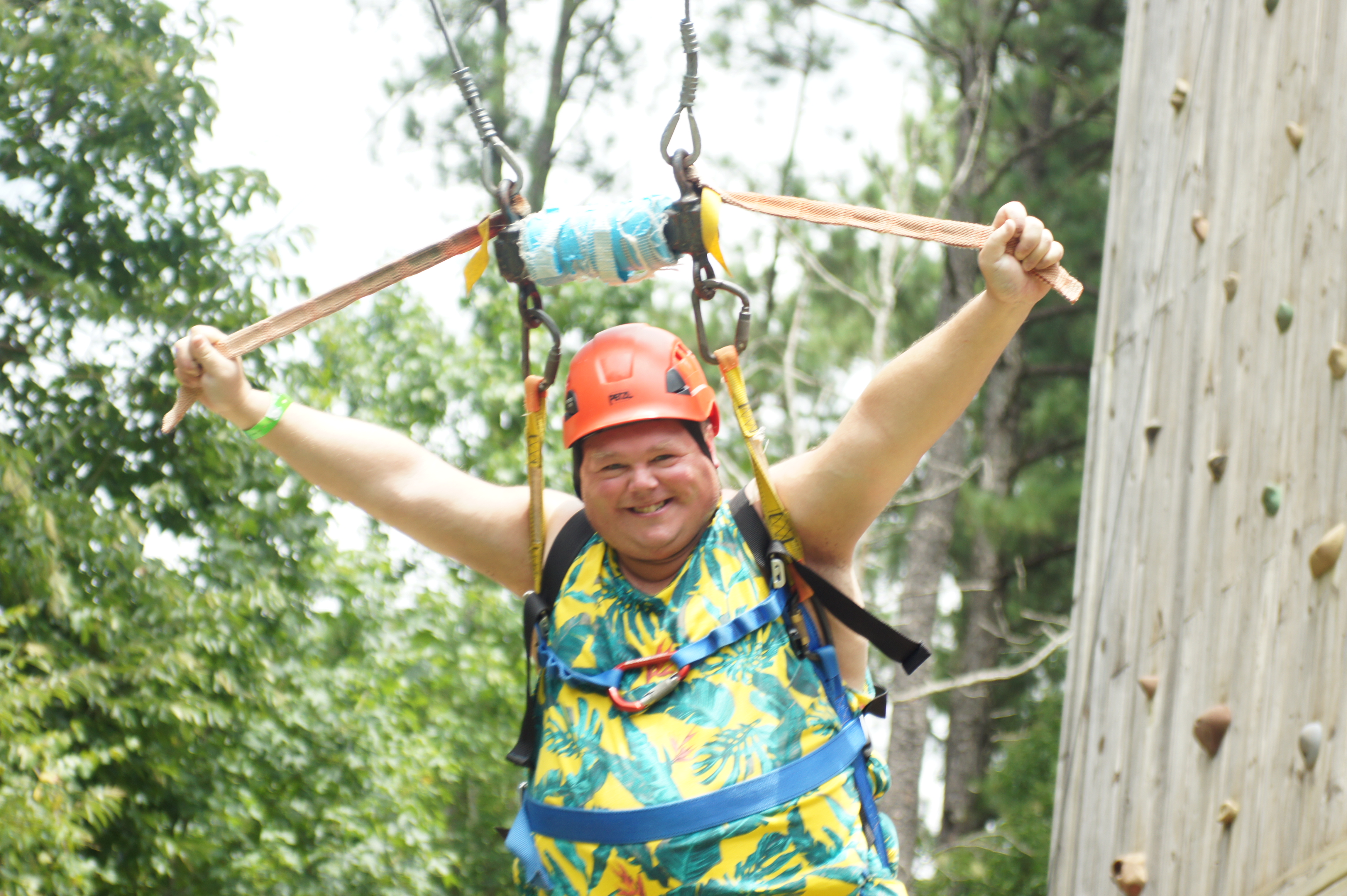 One guy smiling as he swings down a zip line behind a climbing wall