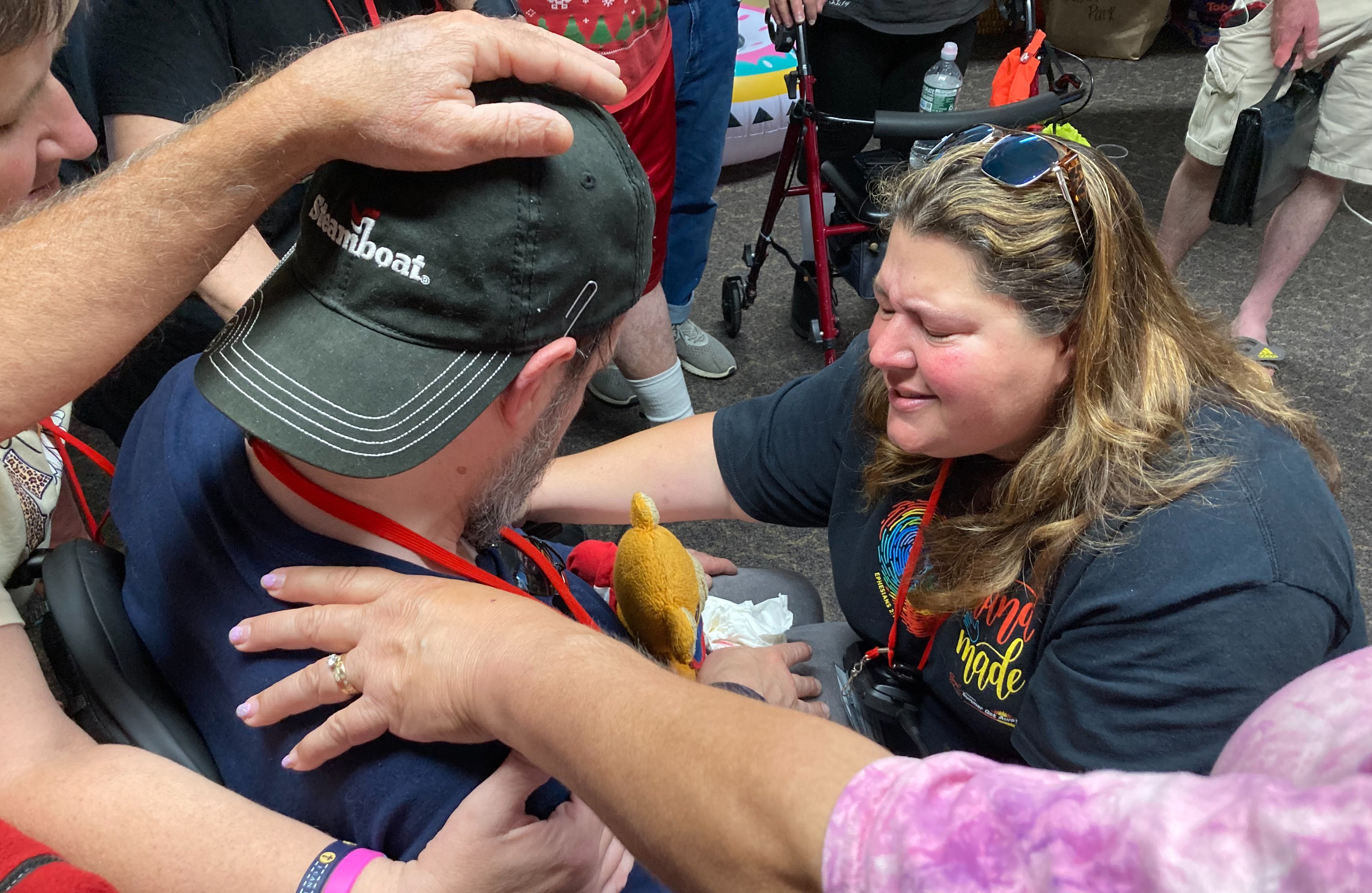 a few people praying with a man sitting in a wheelchair