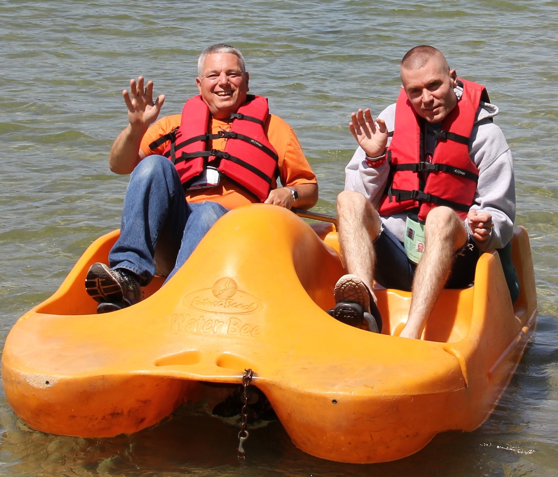 two men waving on a paddleboat on the lake