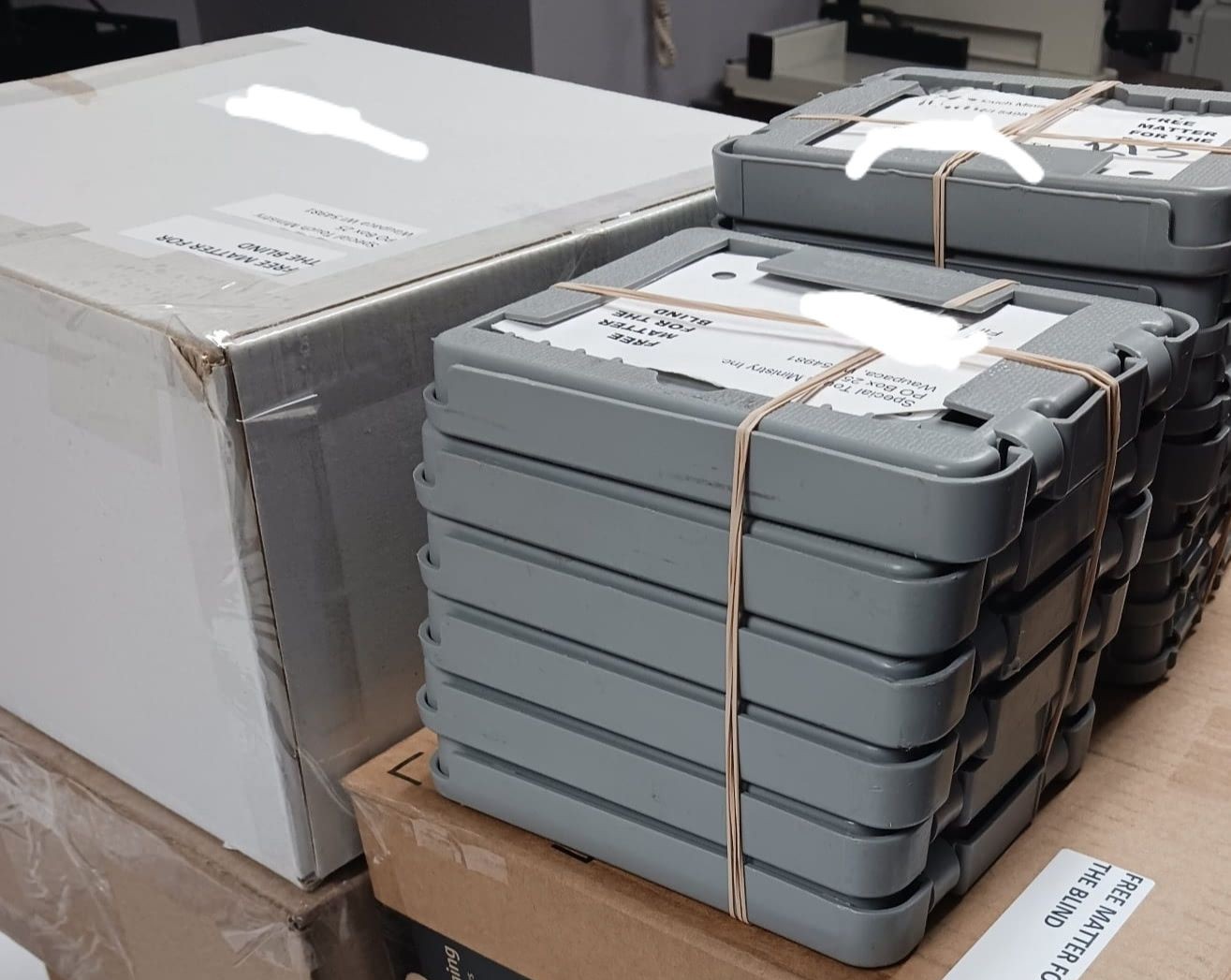 Boxes of materials and digital talking book cartridges all stacked addressed and tagged with Free Matter For the Blind Labels to go out in the USPS