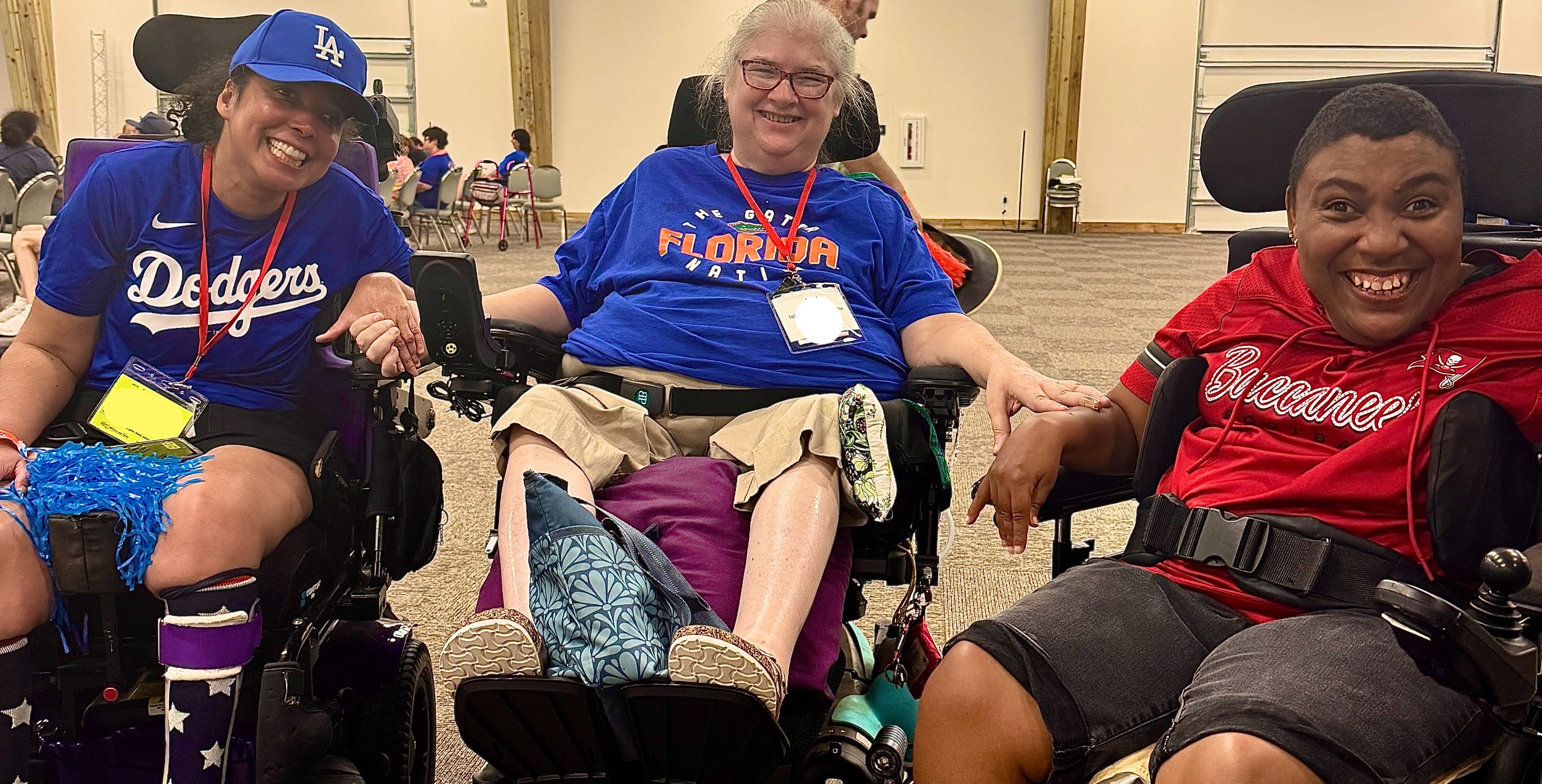 Three people using wheelchairs, located in a meeting room, smiling and all wearing sporting team shirts in red white and blue