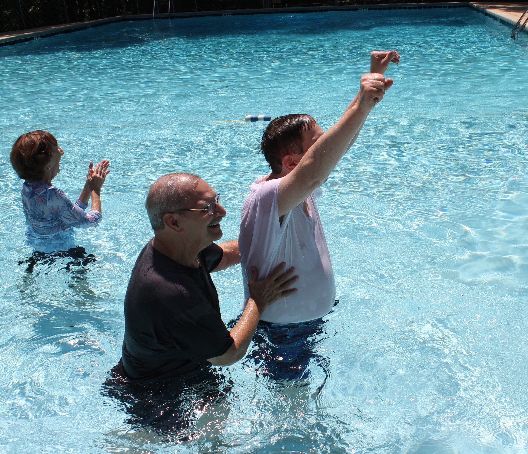 Three people in a pool one with his arms raised after being baptized