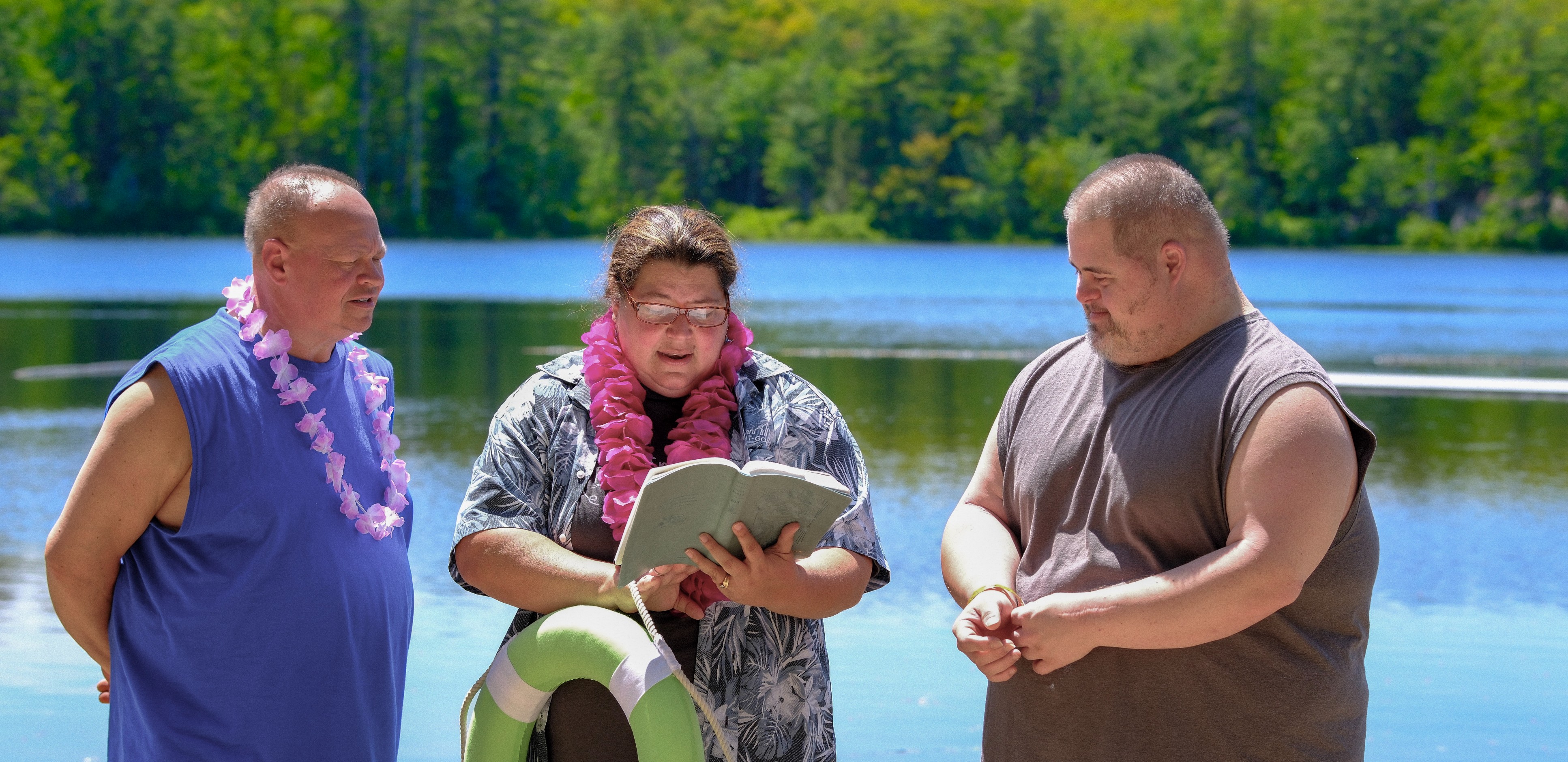 Three people next to a lake one, MA Kim, reading from the bible