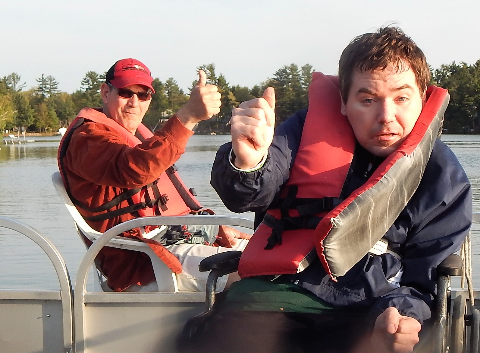 Two men in a boat on a lake with thumbs up one of them is sitting in a wheelchair