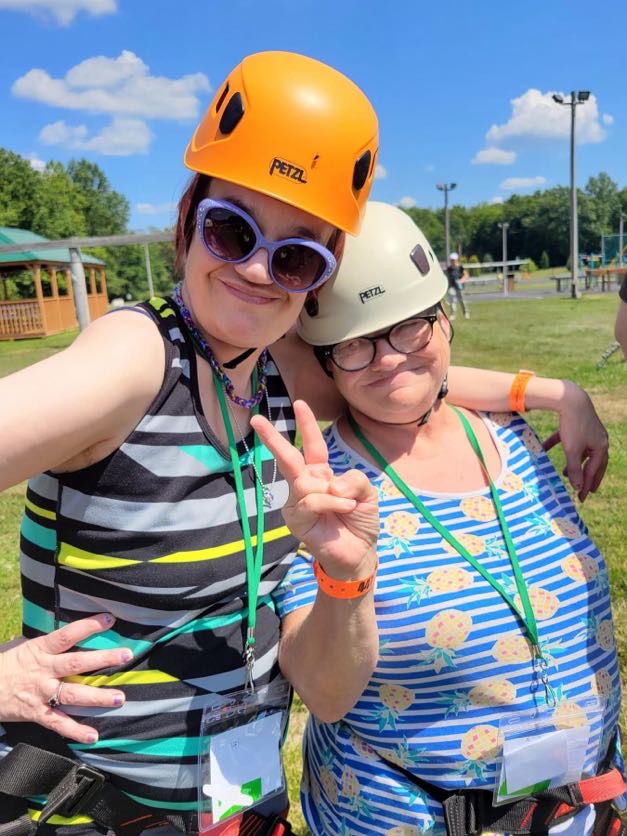 Two women outside wearing climbing gear one with two fingers in a peace sign