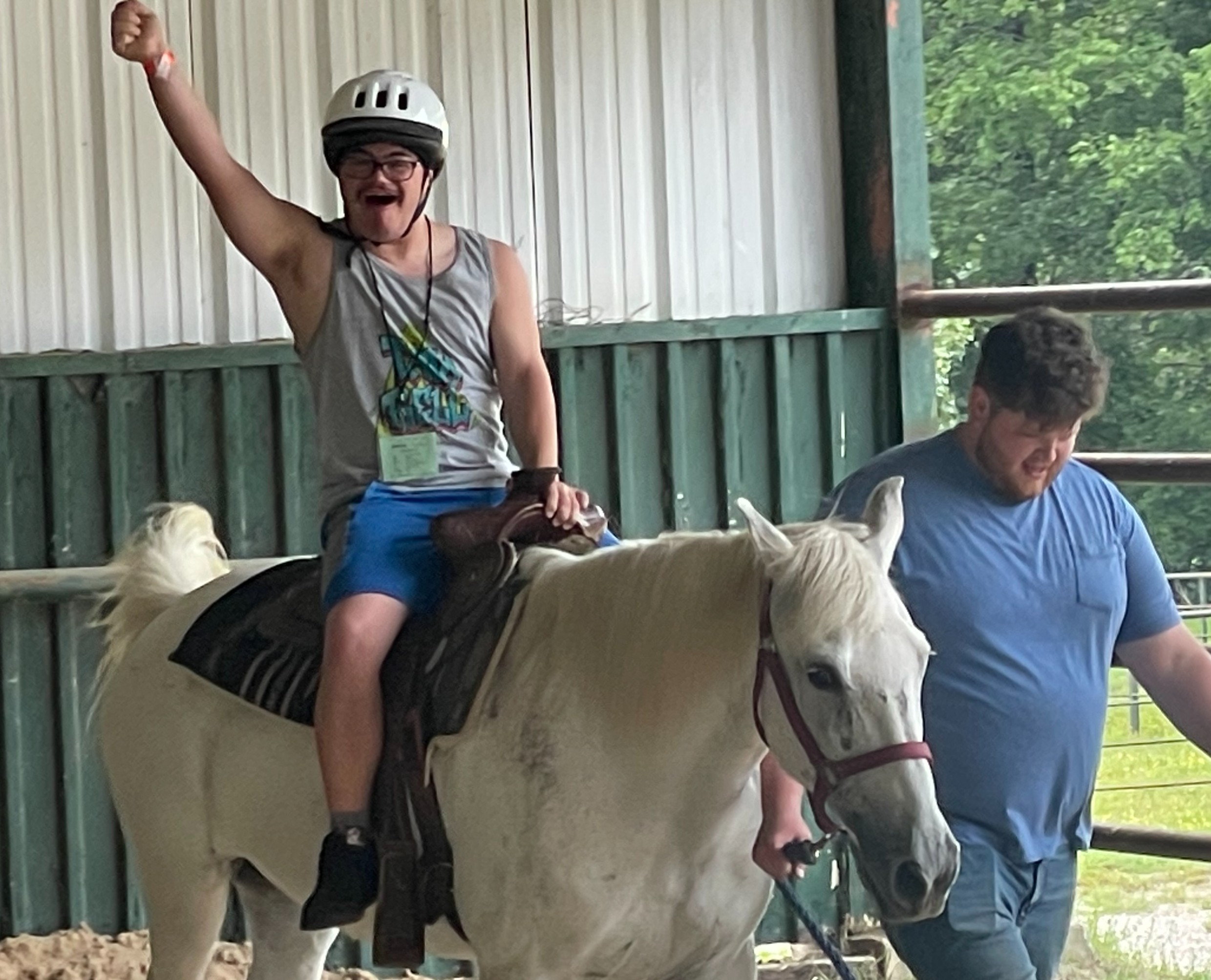 Man with arm in the air cheering while riding a horse with staff person walking nearby holding a lead rope