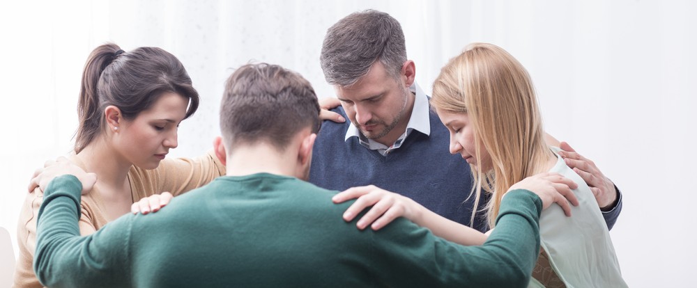 Group of people in a circle holding each other's shoulders while praying together.