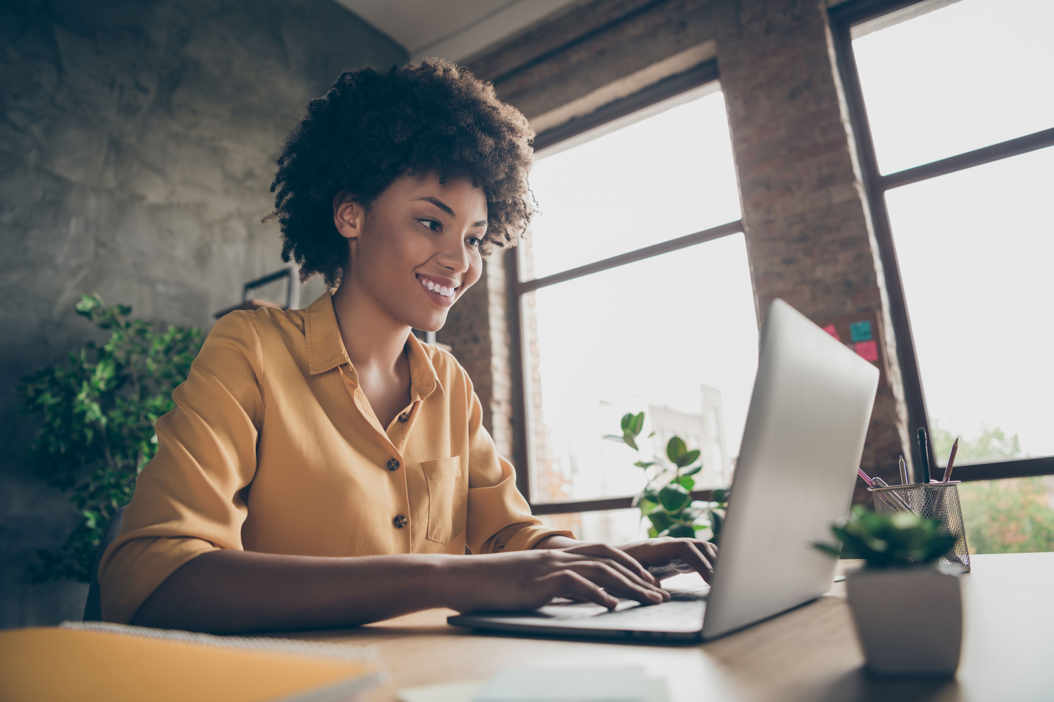 A woman sitting at a desk with a laptop computer. She is looking at the computer and smiling.