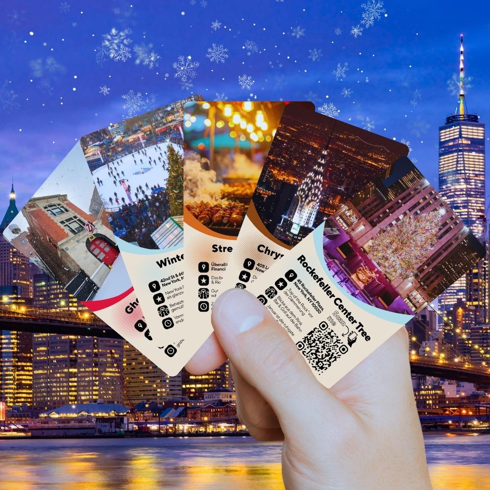 Entdeckerkarten „New York im Winterzauber“ fächerweise in der Hand vor winterlicher NYC-Skyline