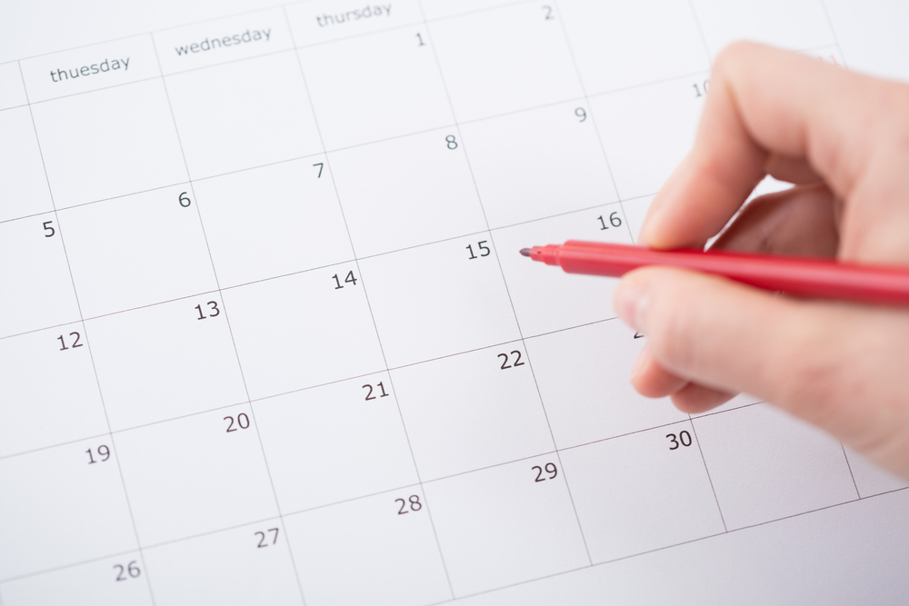 Hand with pen in hand hovering over a open calendar.