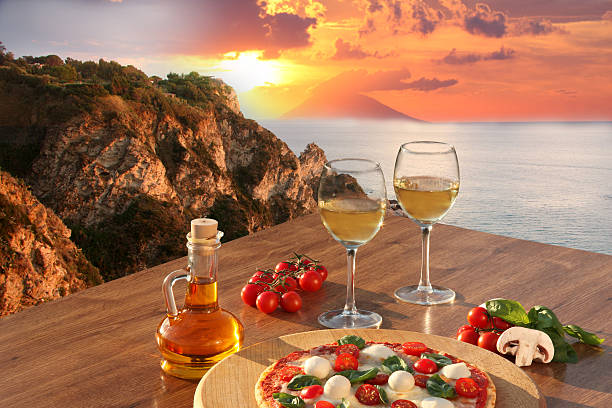 Two glasses of wine and fresh pizza overlooking a beautiful sunset beach view in Sicily, Italy
