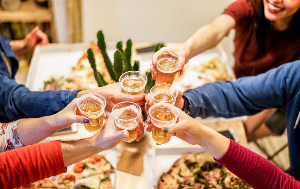 Group of happy friends cheering at home with beer - Young people having fun together eating italian pizza take away - Dinner