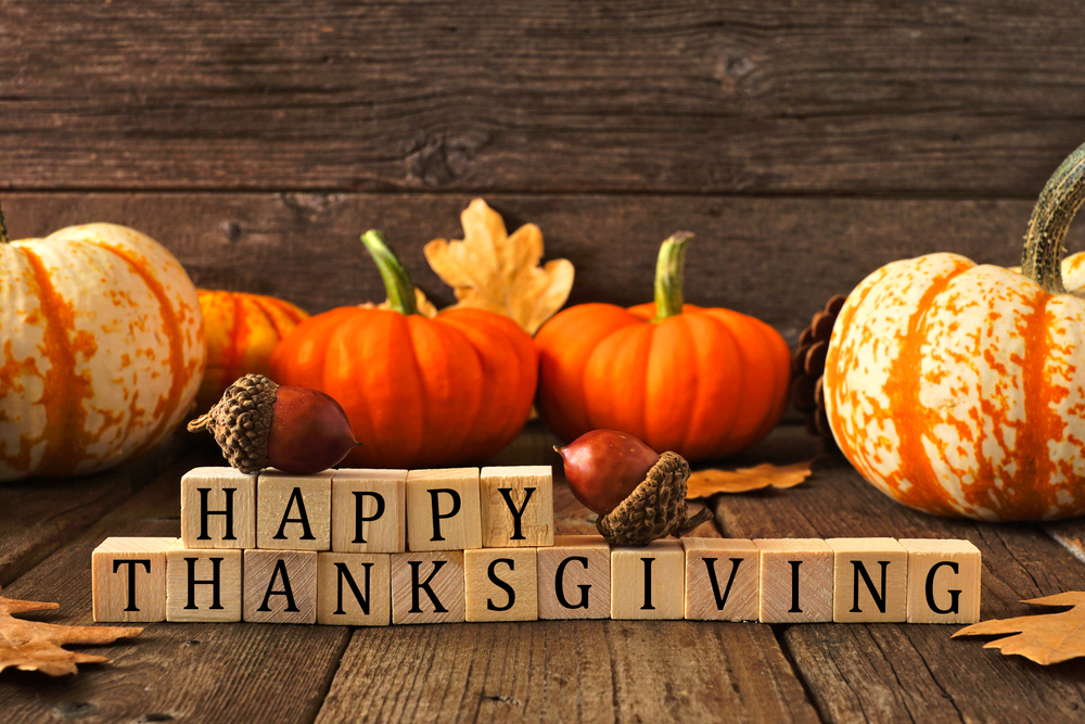 Happy Thanksgiving greeting on wooden blocks against a rustic wood background with pumpkins and autumn leaves