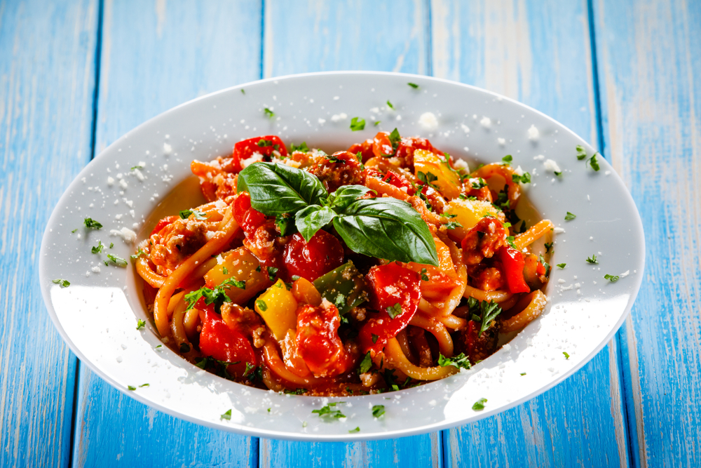 Pasta with meat, tomato sauce and vegetables on wooden table.