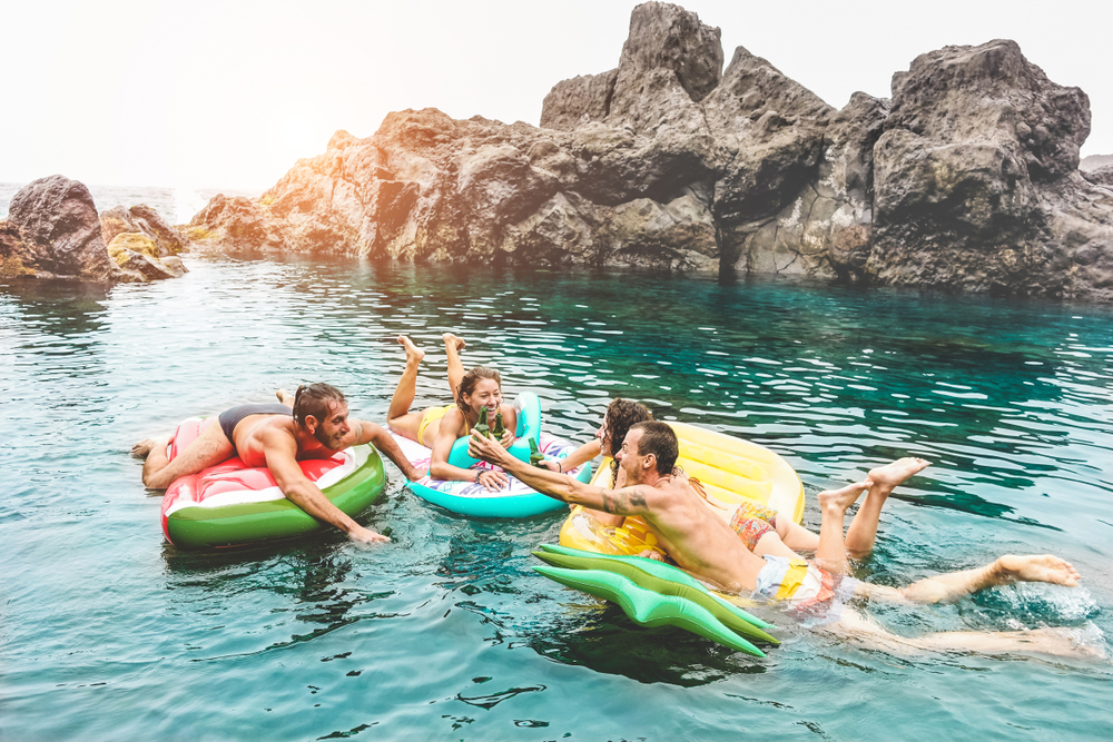 people on rafts having fun in the sea with rock formation in background 