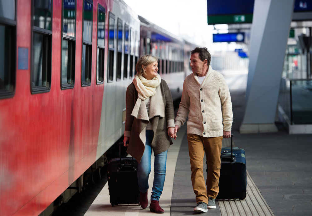 Senior couple on train station pulling trolley luggage.