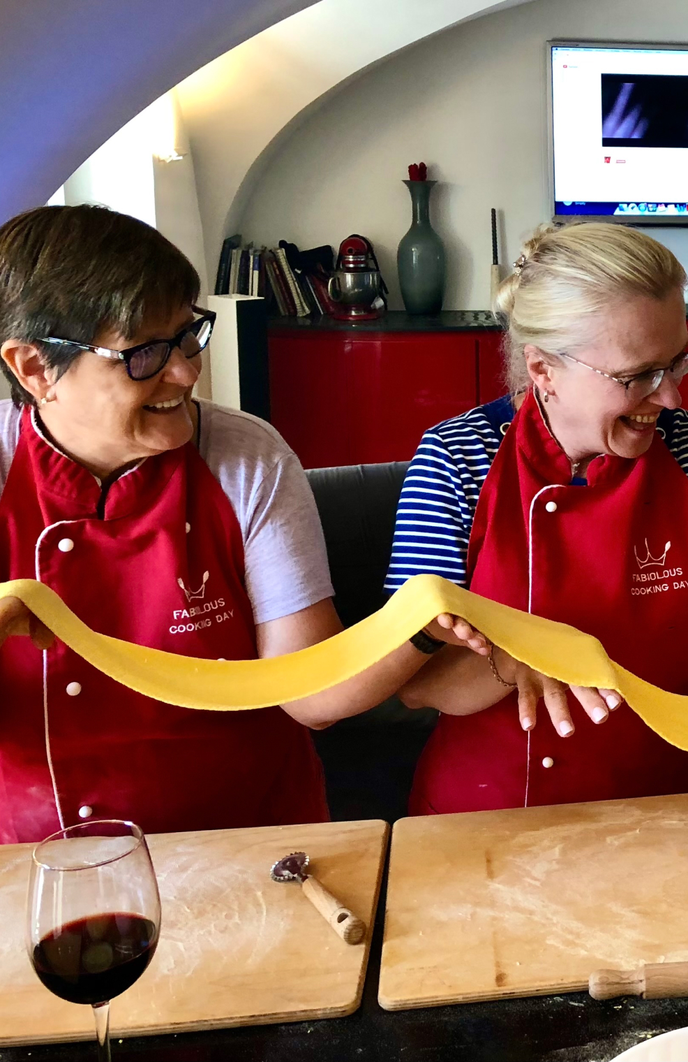 Cooking class with two women holding long noodles in red aprons 