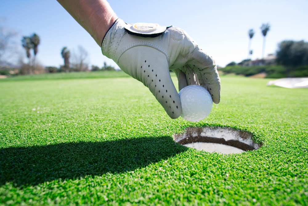 Close-up shot of a person taking golf ball out of the hole on putting green with a focus on hand and golf glove.