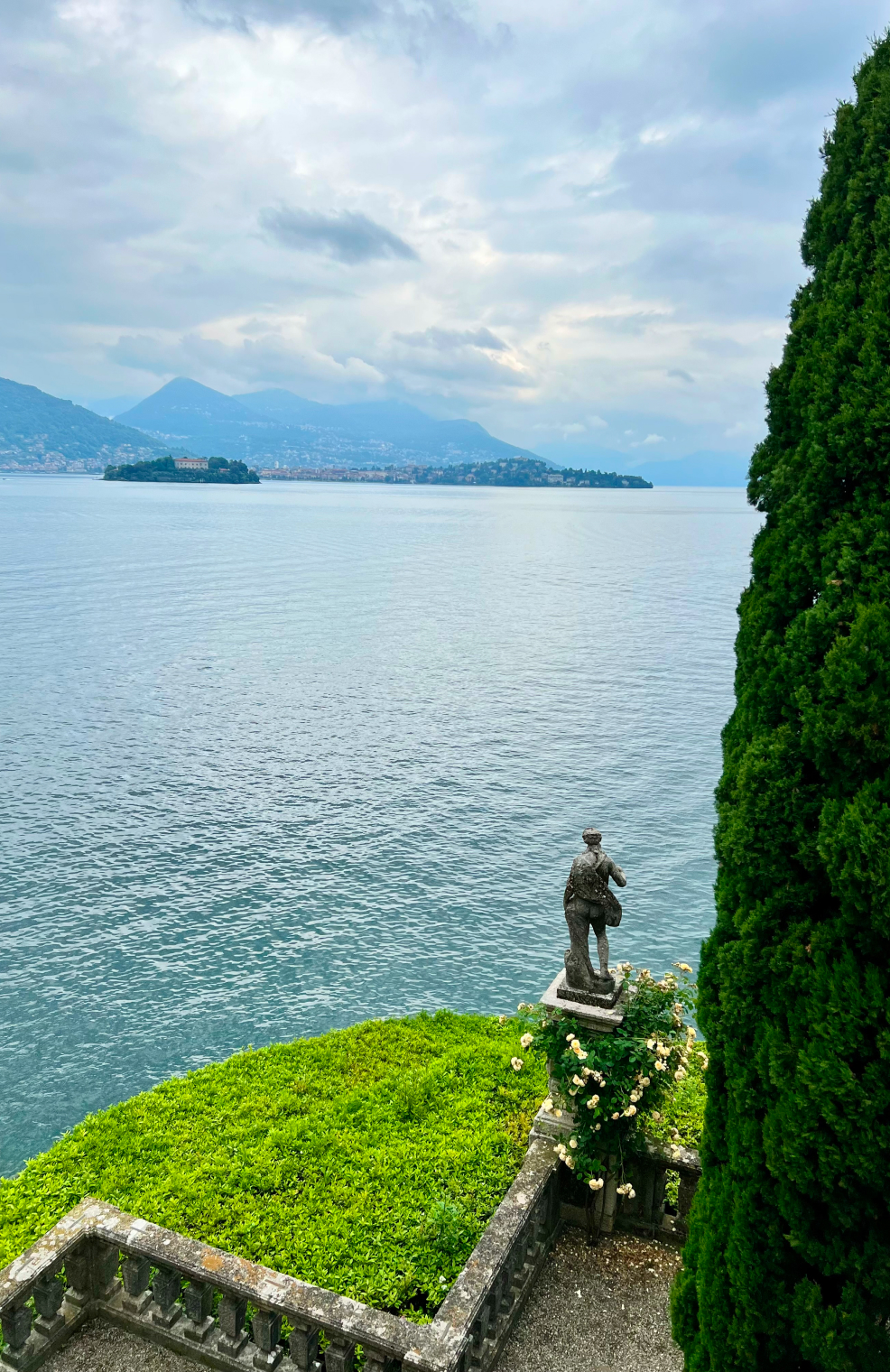 a statue and green tree along the shore of Lake Maggiore