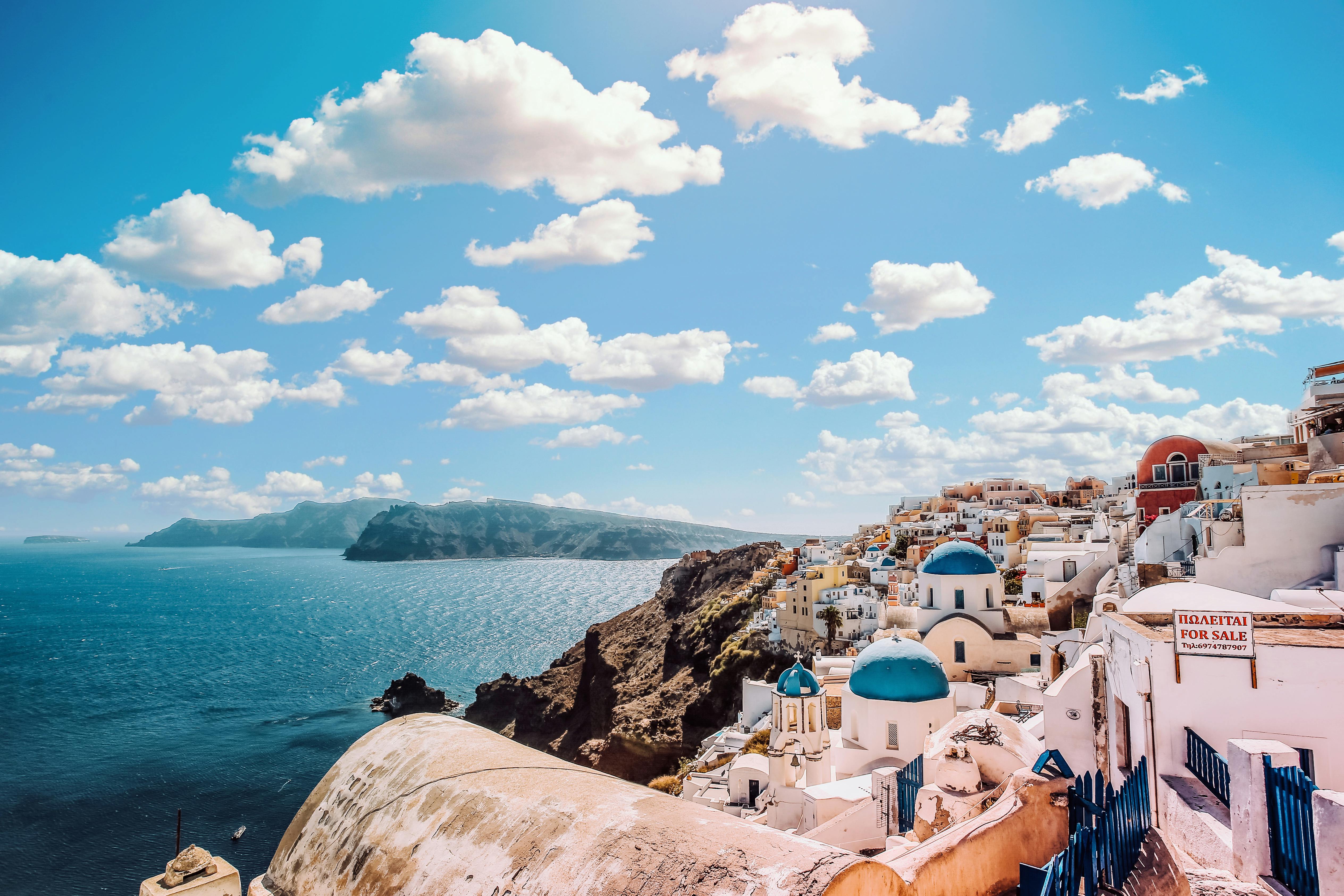 White Concrete House Near Body of Water Under White and Blue Cloudy Sky In Santorini