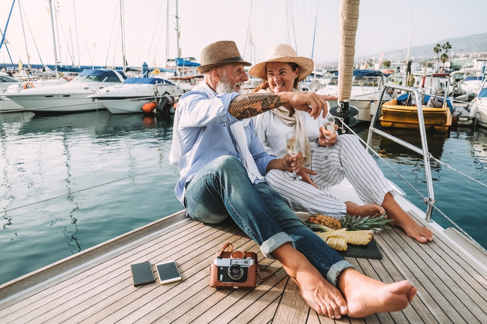 A older couple sitting on a dock with wine surrounded by boats