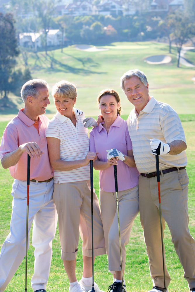 Portrait of smiling mature couple with friends on golf course together.