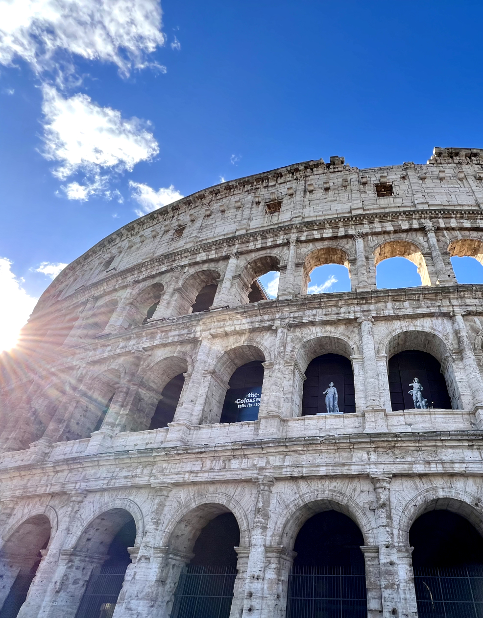 photo of the colosseum in Rome with blue sky and sun rays