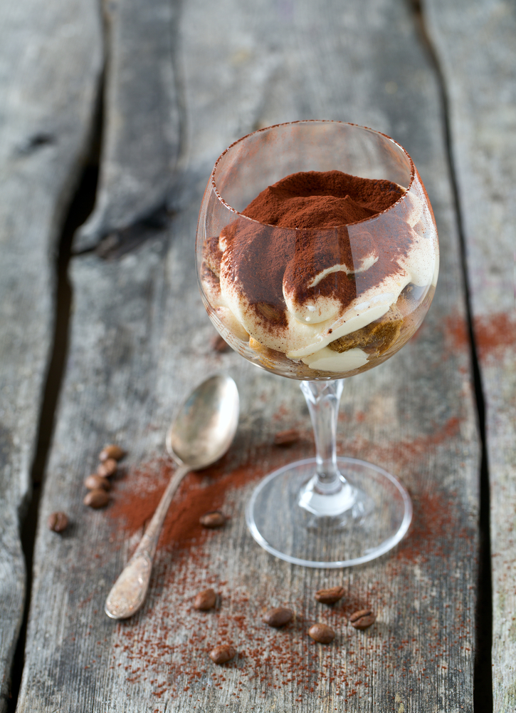 tiramisu in a vine glass on wooden surface