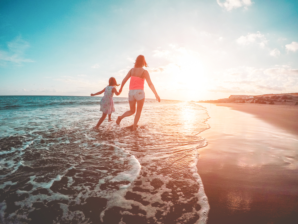 A mother and child running in the seashore with sunset in background