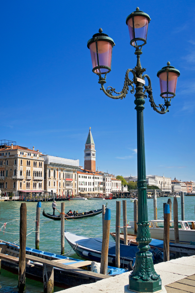 Streetlight and gondola on the sunny Grand Canal in front of San Marco Campanile and architectural buildings in Venice, Italy.