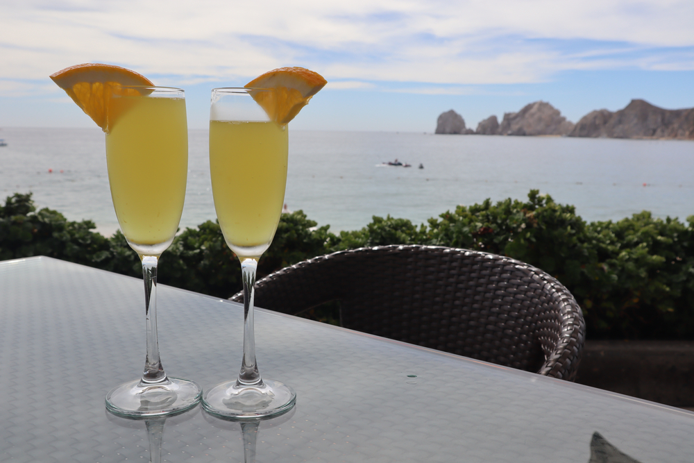 A closeup of glasses of two mimosas with orange slice garnish overlooking the bay and the cape