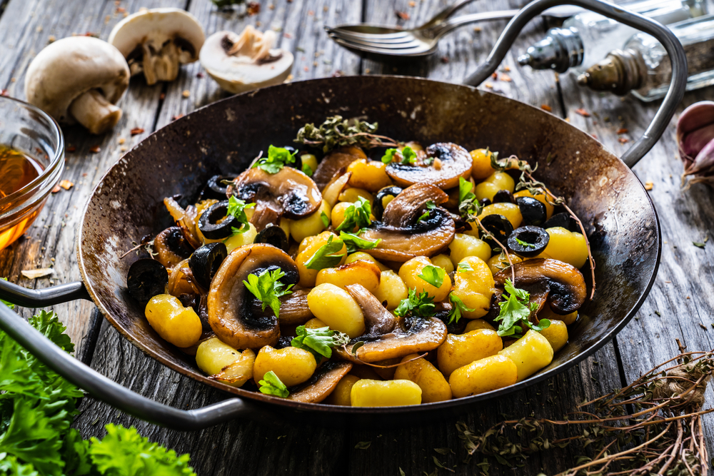 Gnocchi with fried white mushrooms on wooden table.