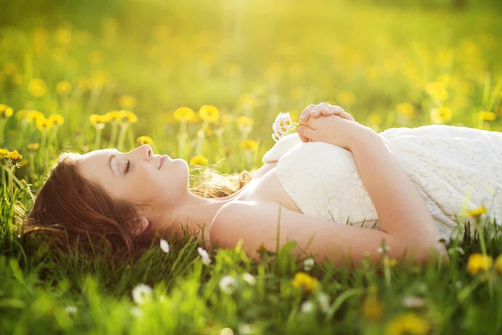 Femme souriante se reposant couchée dans l'herbe les yeux fermés