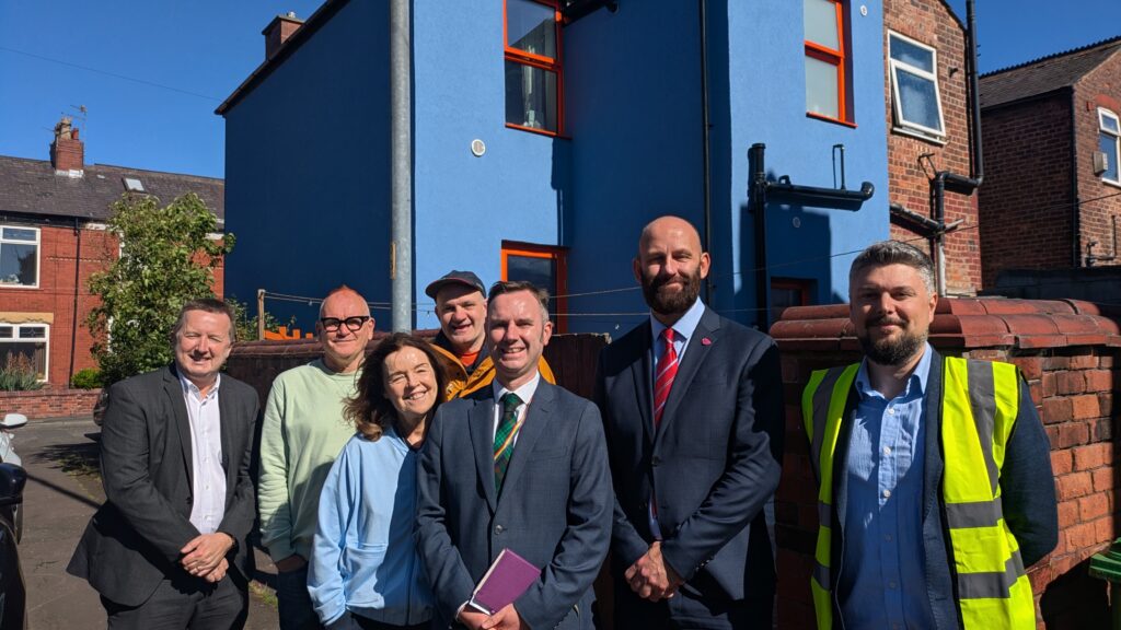 A photo of Jonathan Atkinson, B4Box Partners, and a Levenshulme Area Based Scheme householder standing alongside Traffor Council Leader, and Salford Mayor outside a home that has had blue external wall insulation fitted.