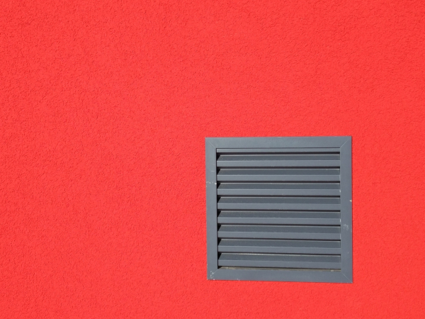 A photo of a square grey vent on a red painted wall