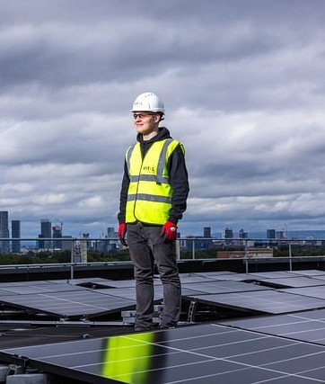 A man wearing a hard hat and hi-vis standing on a roof by solar panels