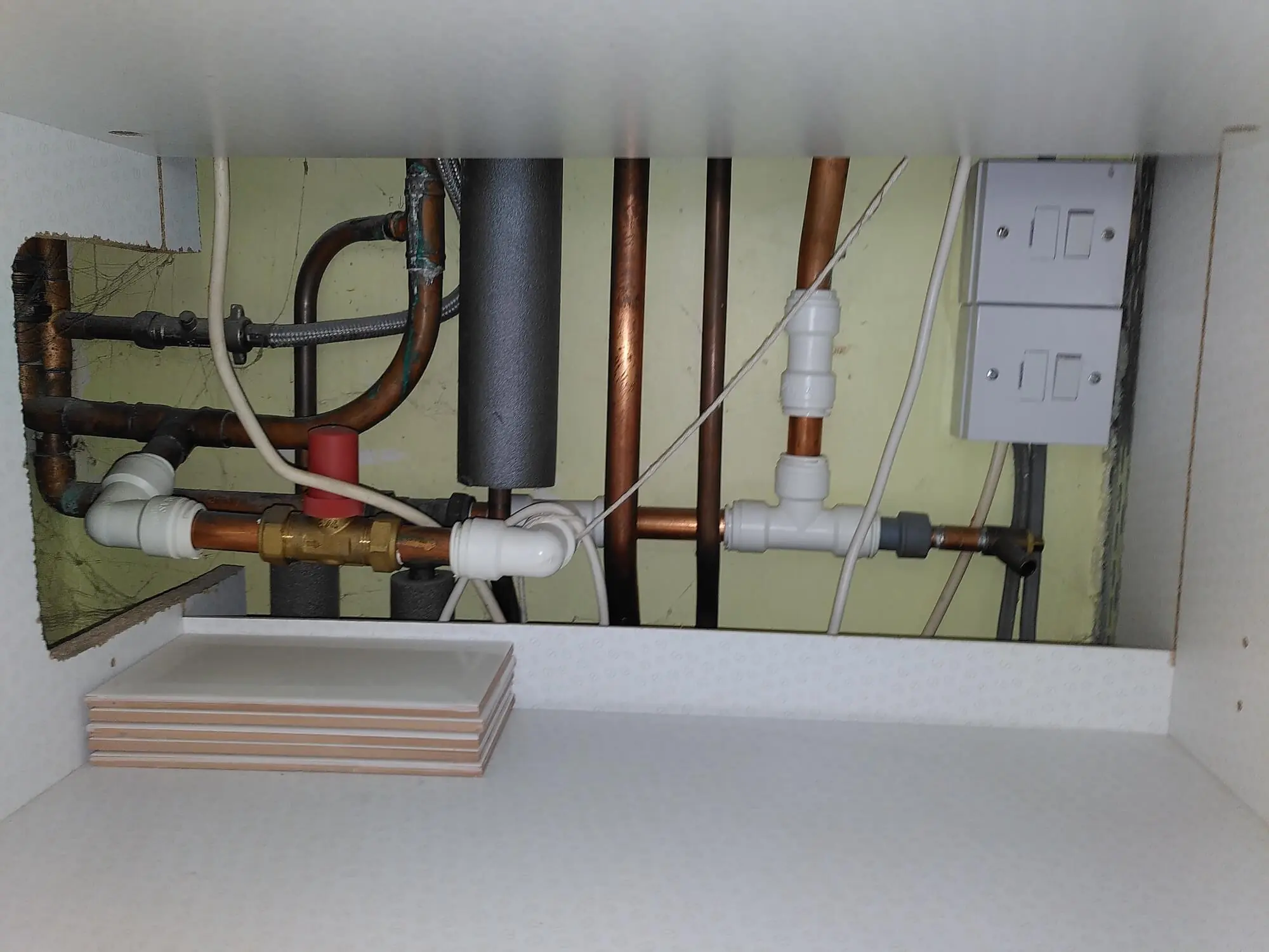 A photo of some concealed (in a cupboard) pipework and electrical wires