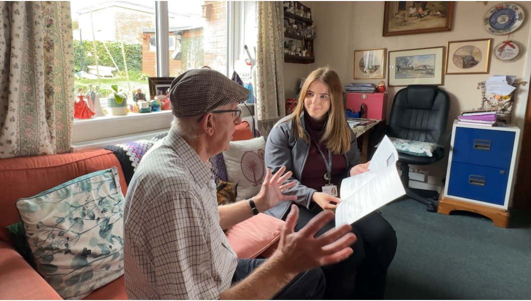 A photo of a resident liaison officer in a tenant's living room, showing them retrofit plans