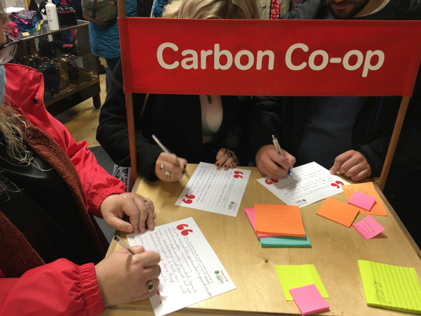People writing on post it notes and postcards in front of a Carbon Co-op banner