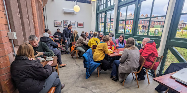 A photo of a room full of people meeting in a cafe space around several tables