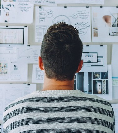 A photo of the back of a man's head looking towards a wall of various planning documents