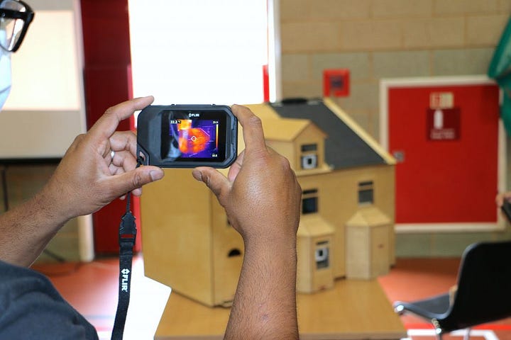 Someone pointing a thermal imaging camera at a model 'energy house'. 