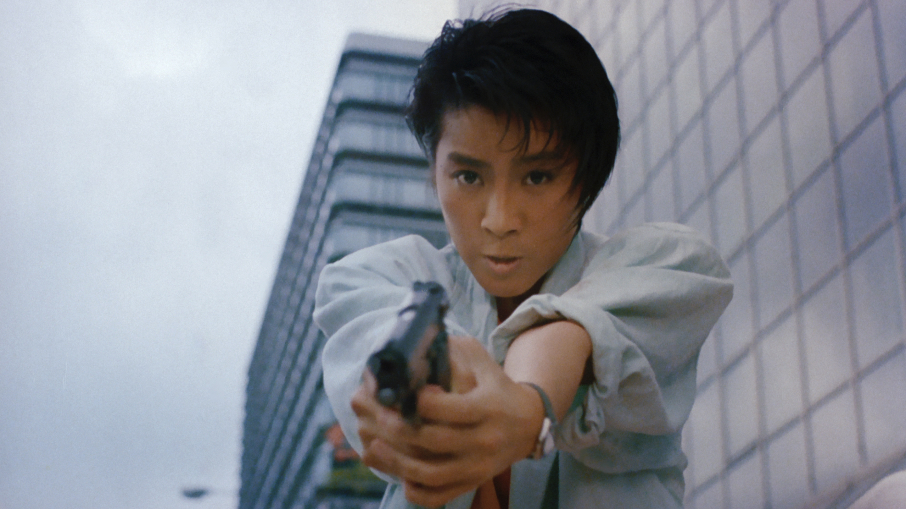 an asian woman in a white suit pointing a gun towards the camera