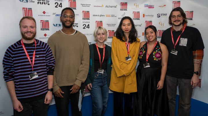 six smiling young people infront of a cambridge film festival sponsors board