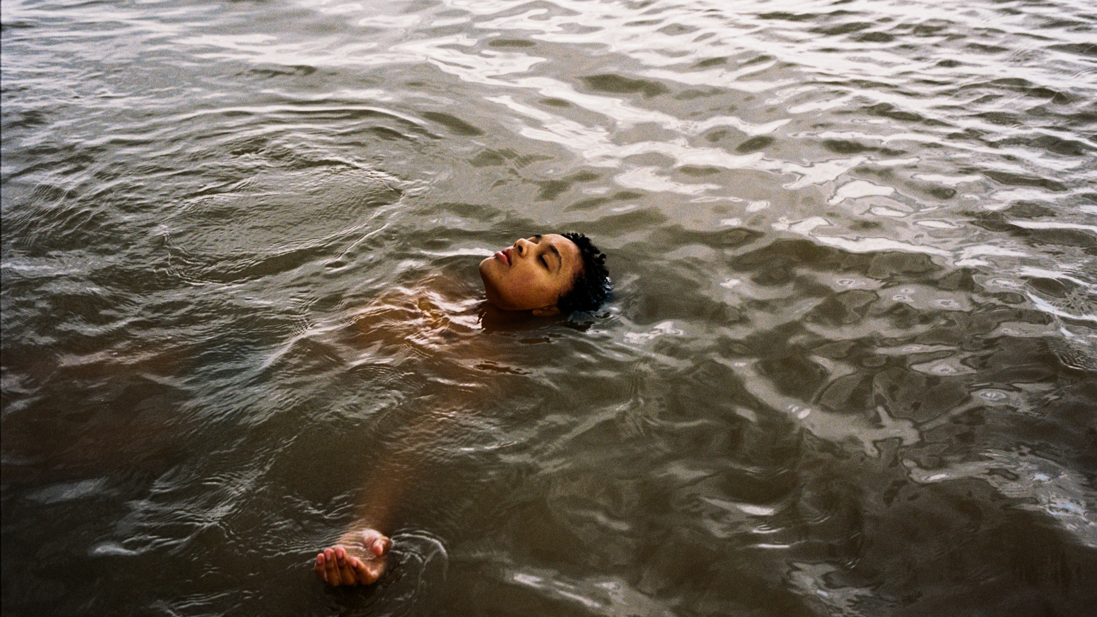 young woman floating peacefully on her back in rippling water