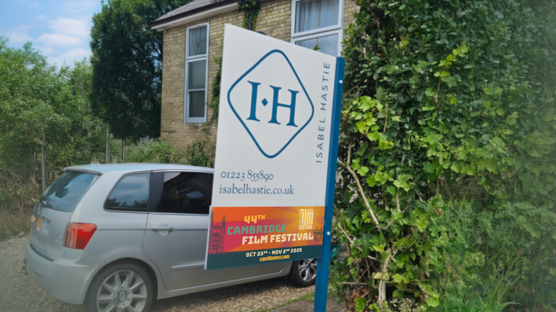 an estate agent sign in front of a house with a silver car.