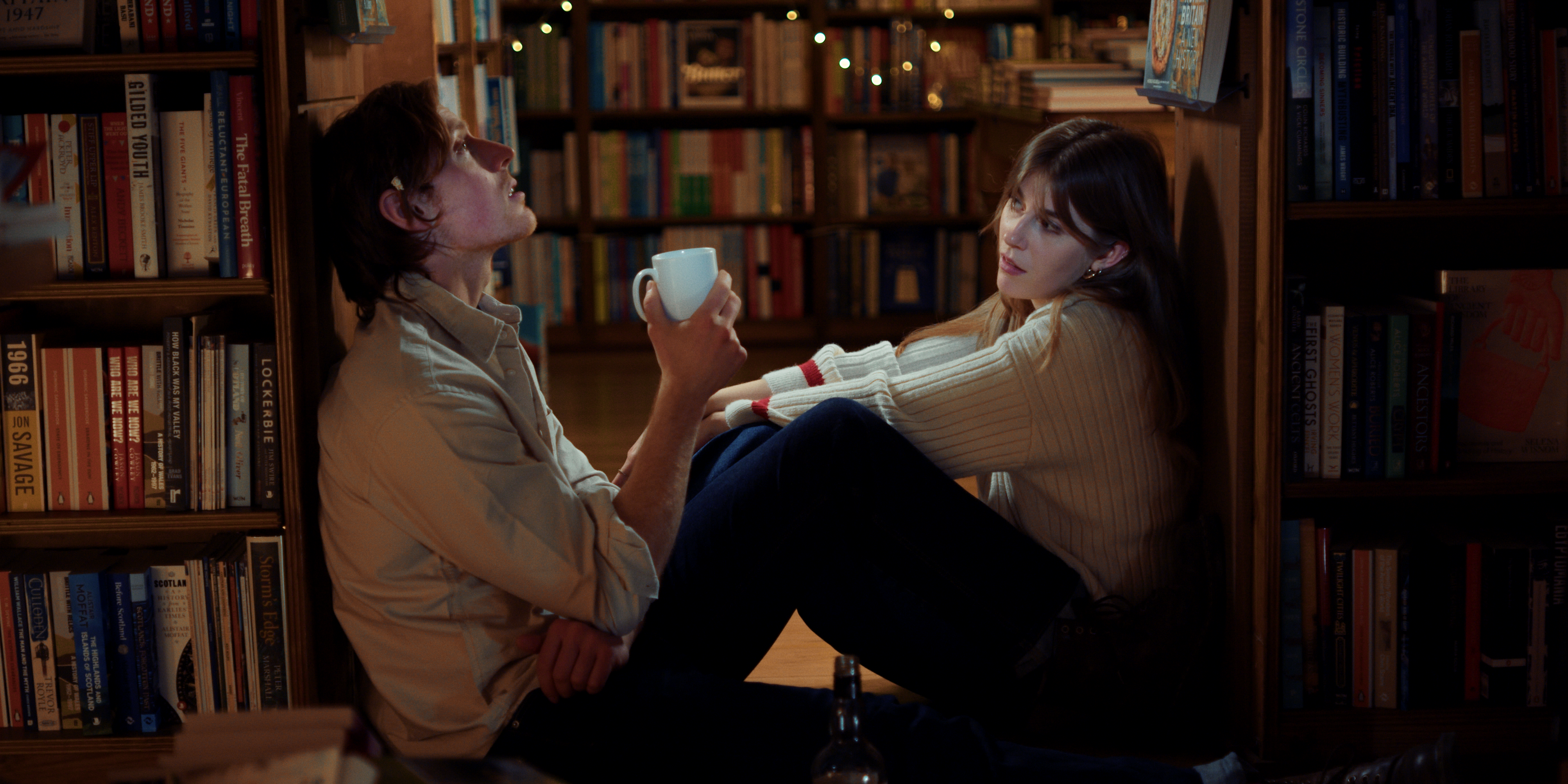 a young man and woman sitting in a dimmly lit bookshop