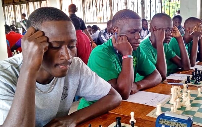 Three Mustard Seed students looking intently at their chess boards with a huge room full of of chess players
